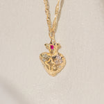 Gold necklace with a heart-shaped pendant featuring a ruby on a light beige background