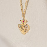 Gold necklace with a heart-shaped pendant featuring a ruby on a light beige background