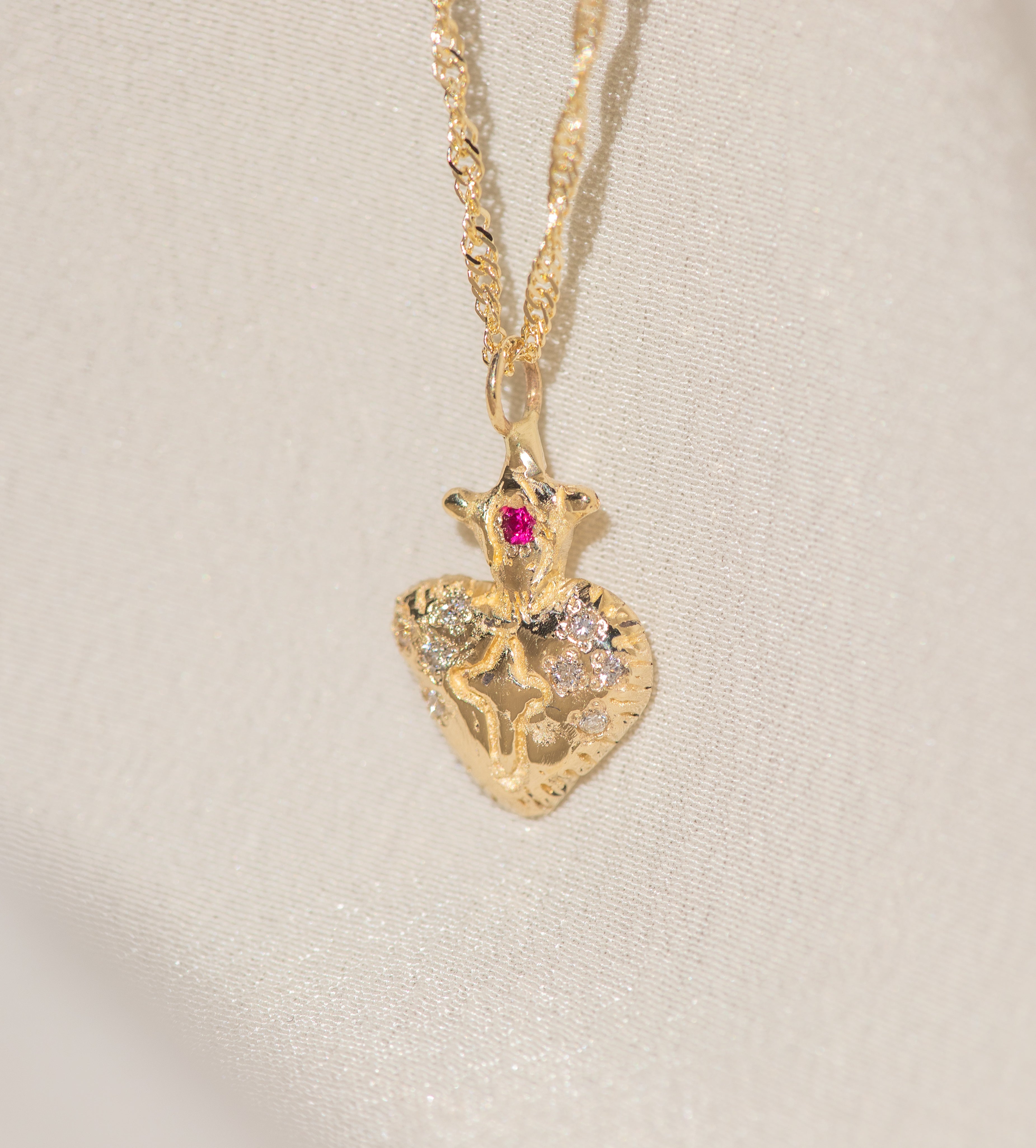 Gold necklace with a heart-shaped pendant featuring a ruby on a light beige background