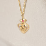 Gold heart-shaped pendant necklace with a red gemstone on a light beige background