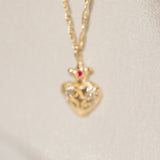 Gold heart-shaped pendant necklace with a red gemstone on a light beige background