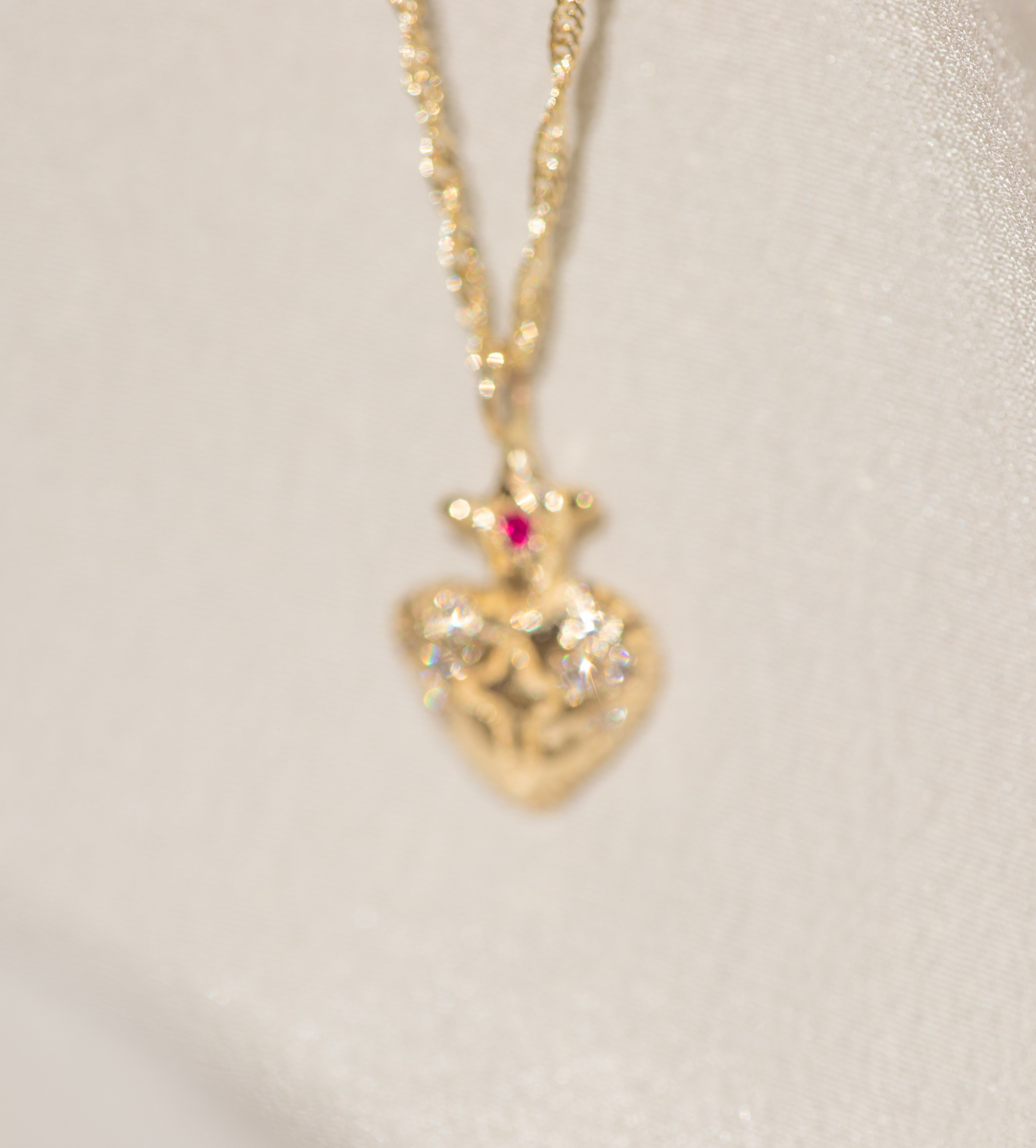 Gold heart-shaped pendant necklace with a red gemstone on a light beige background