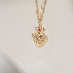 Gold heart-shaped pendant necklace with a red gemstone on a light gray background