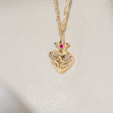 Gold heart-shaped pendant necklace with a red gemstone on a light gray background