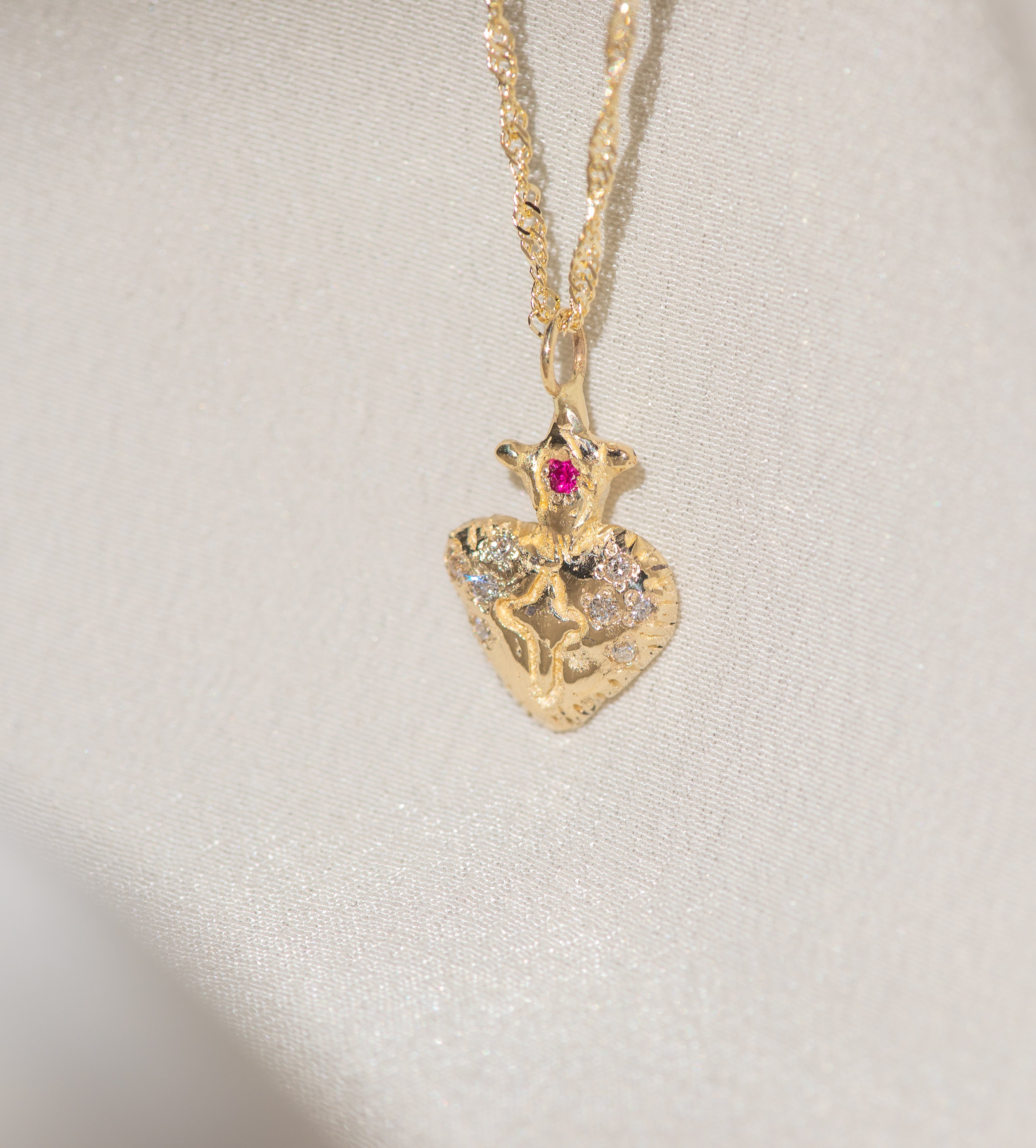 Gold heart-shaped pendant necklace with a red gemstone on a light gray background