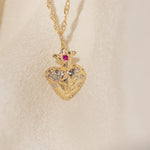 Gold heart-shaped pendant with a red gemstone on a beige background