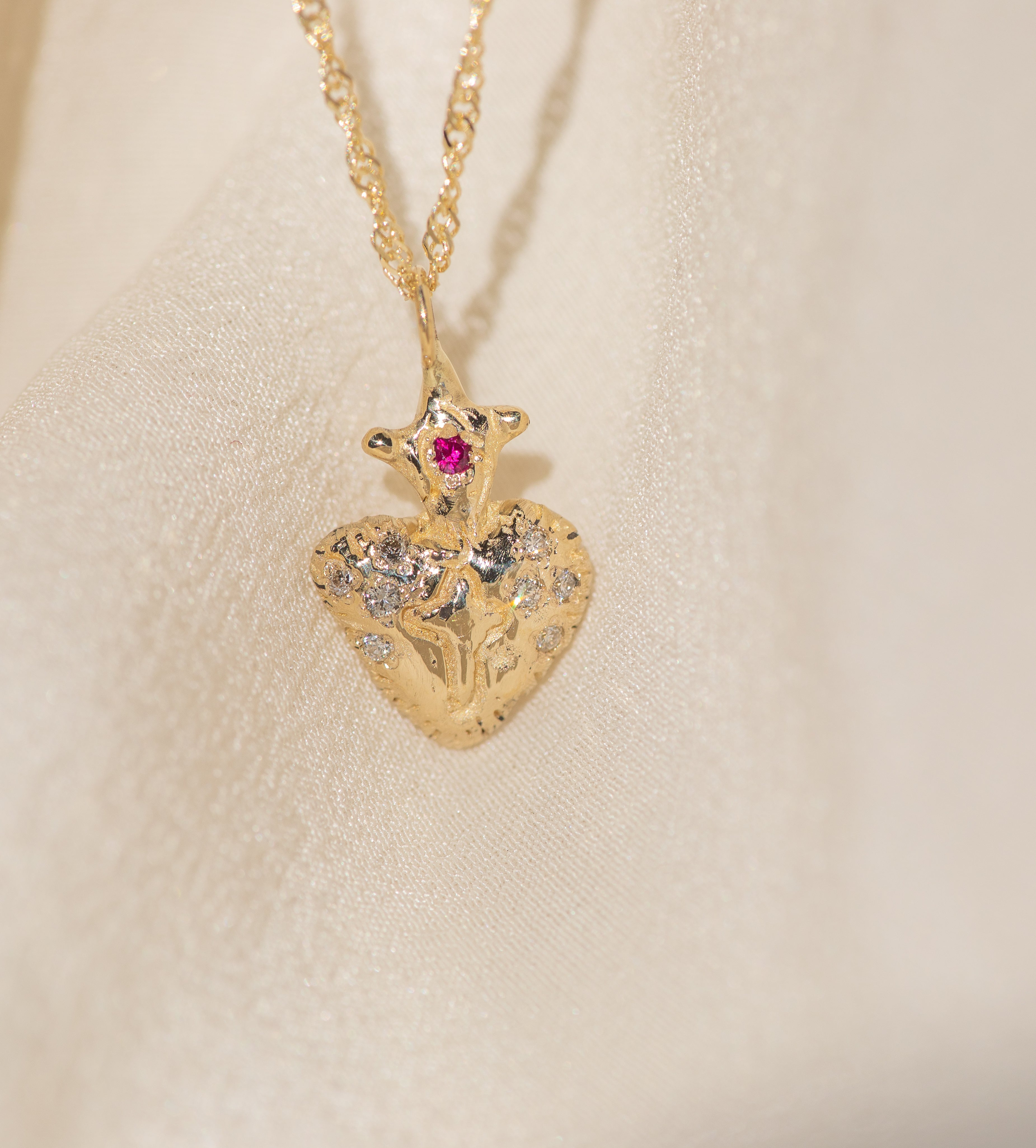 Gold heart-shaped pendant with a red gemstone on a beige background