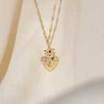 Gold heart-shaped pendant necklace with a red gemstone on an ivory background