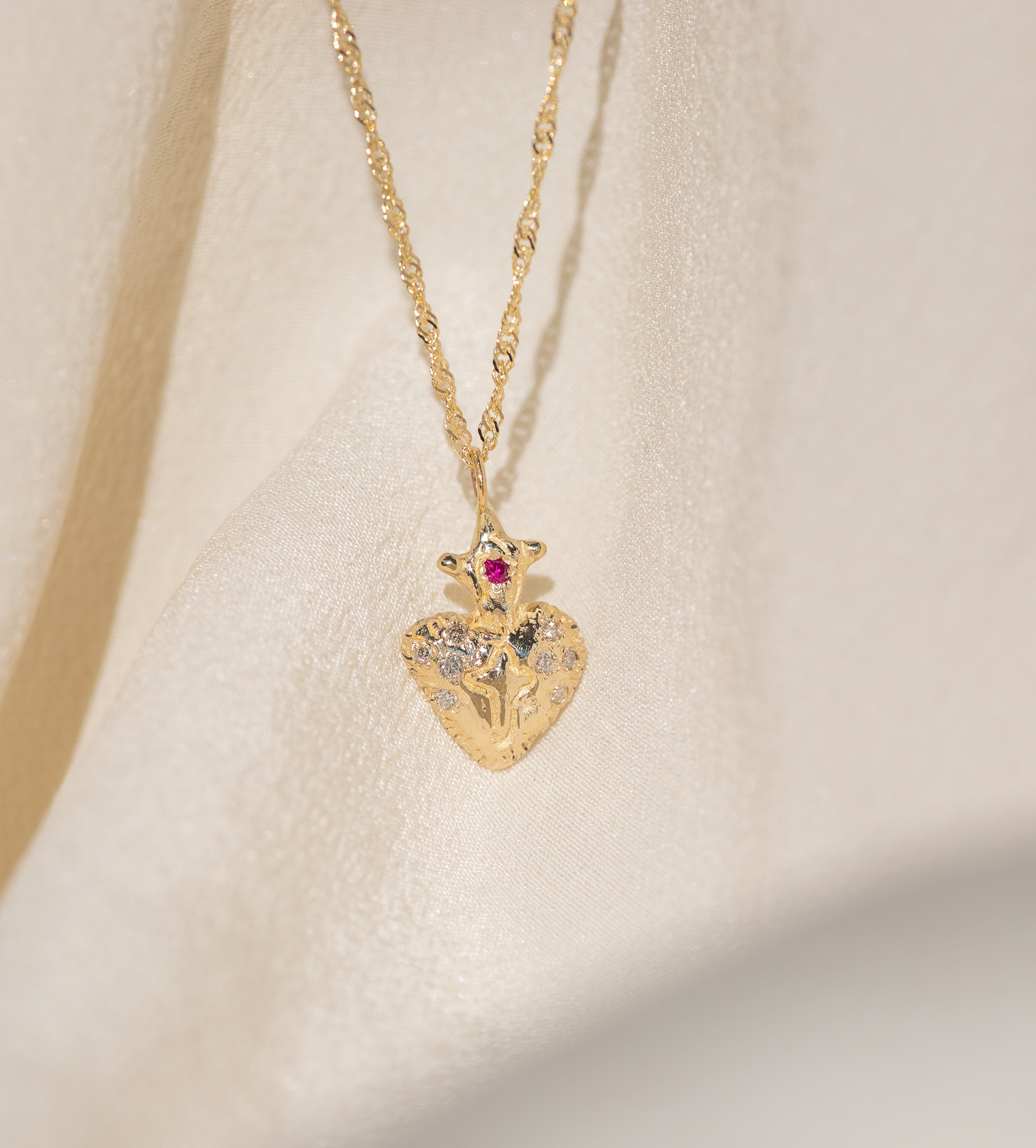 Gold heart-shaped pendant necklace with a red gemstone on an ivory background
