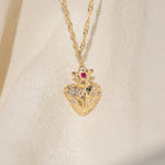 Gold heart-shaped pendant necklace with gemstones on a beige background