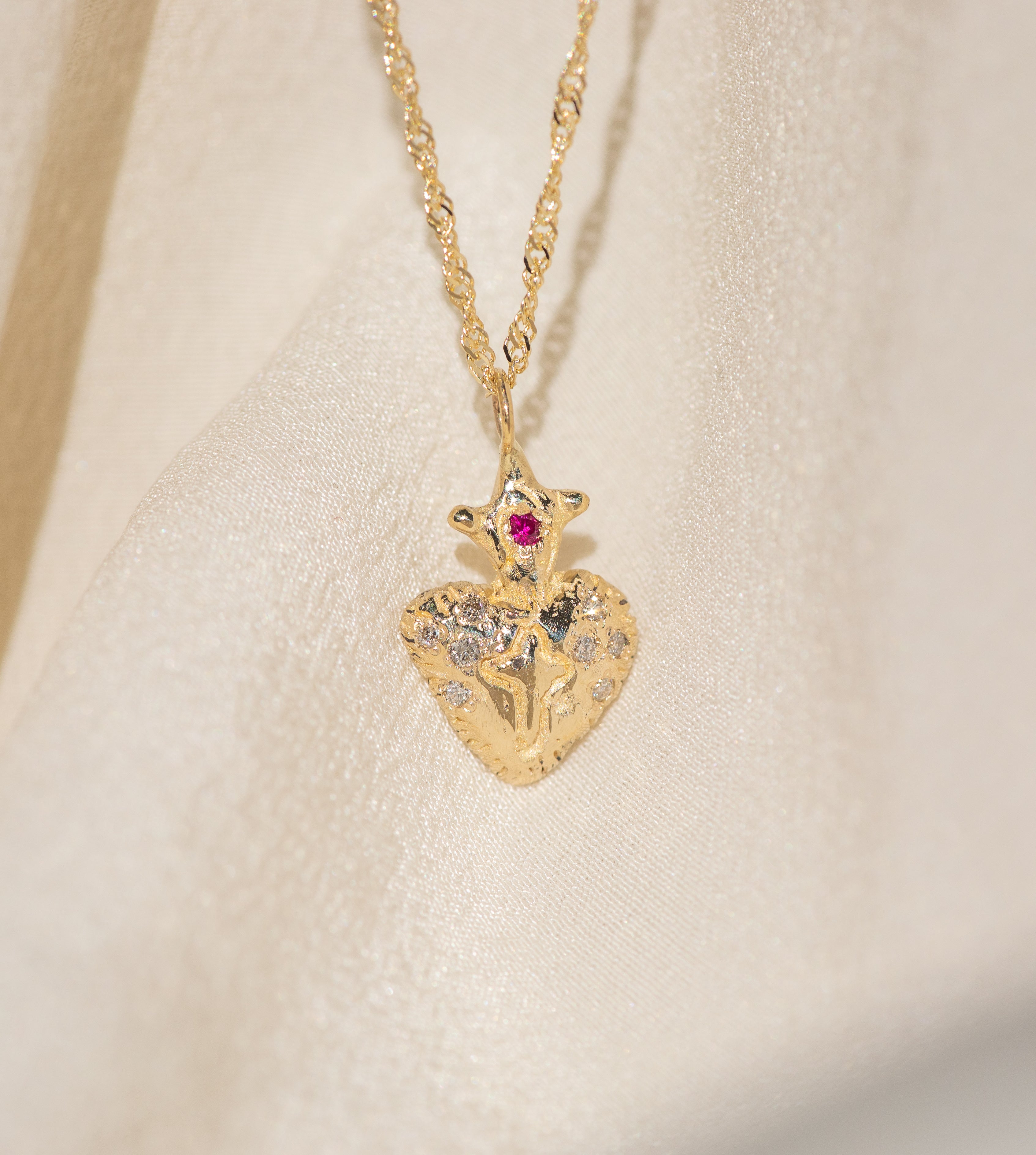 Gold heart-shaped pendant necklace with gemstones on a beige background