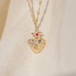 Gold heart-shaped pendant necklace with embedded stones on a beige fabric background