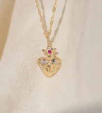 Gold heart-shaped pendant necklace with embedded stones on a beige fabric background
