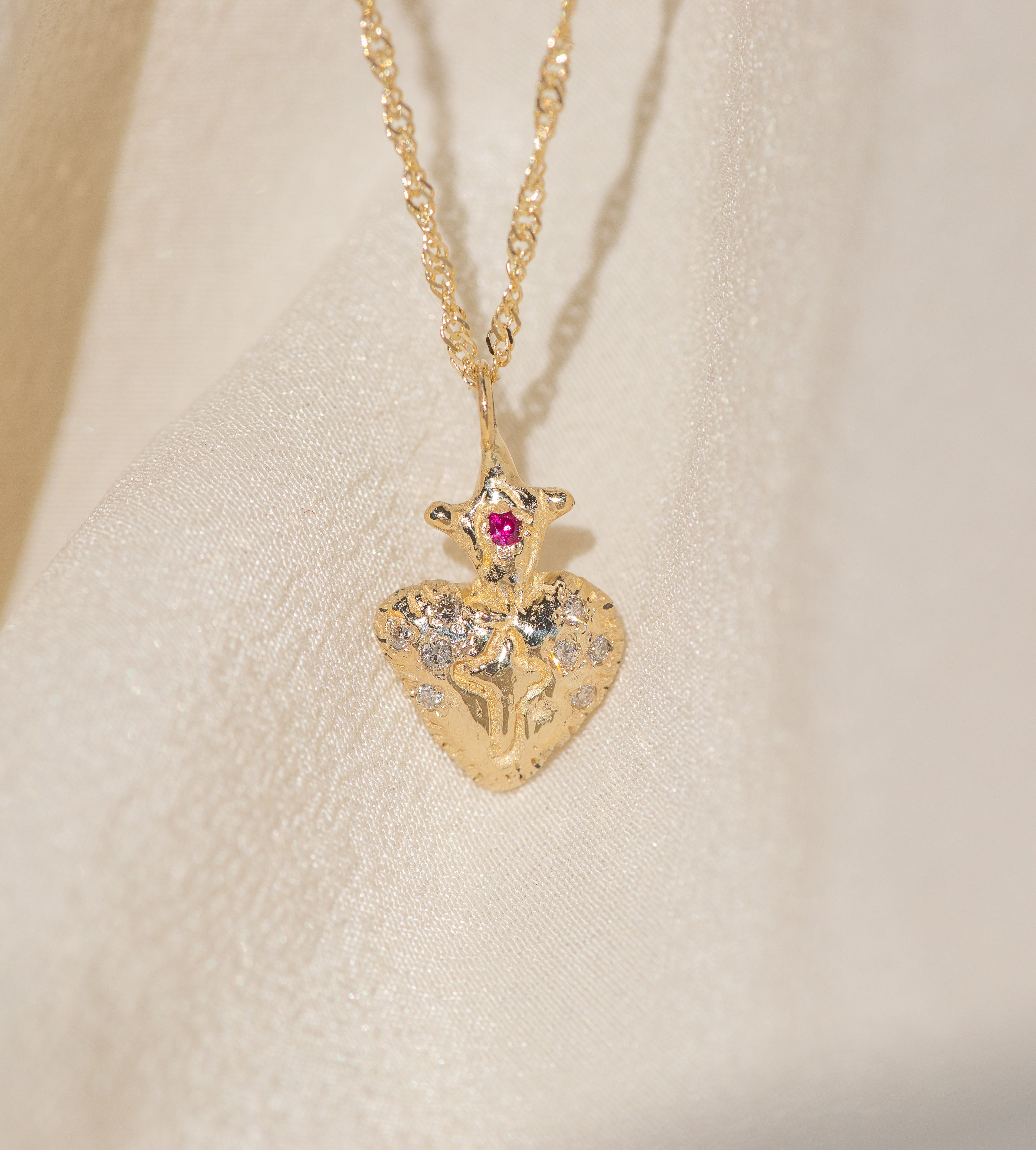Gold heart-shaped pendant necklace with embedded stones on a beige fabric background