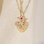 Gold necklace with a heart-shaped pendant featuring a red gemstone on a beige background