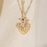 Gold necklace with a heart-shaped pendant featuring a red gemstone on a beige background