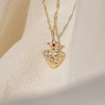 Gold necklace with a heart-shaped pendant featuring a red gemstone on a beige background