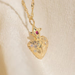 Gold heart-shaped pendant necklace with a red gemstone on a beige background