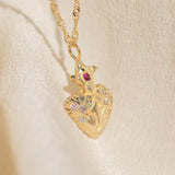 Gold heart-shaped pendant necklace with a red gemstone on a beige background