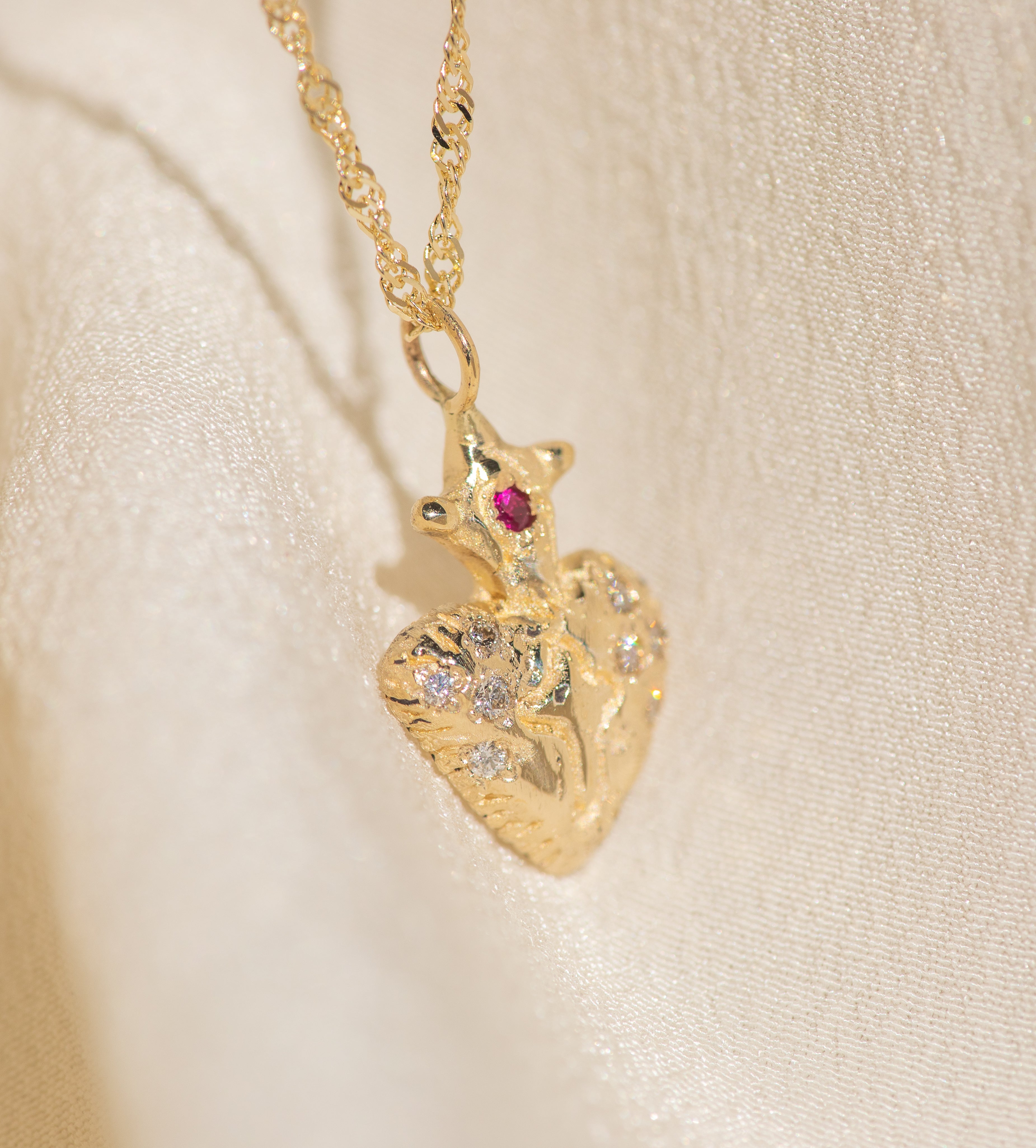 Gold heart-shaped pendant necklace with a red gemstone on a beige background
