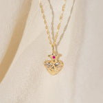 Gold heart-shaped necklace with a red gemstone on a beige background