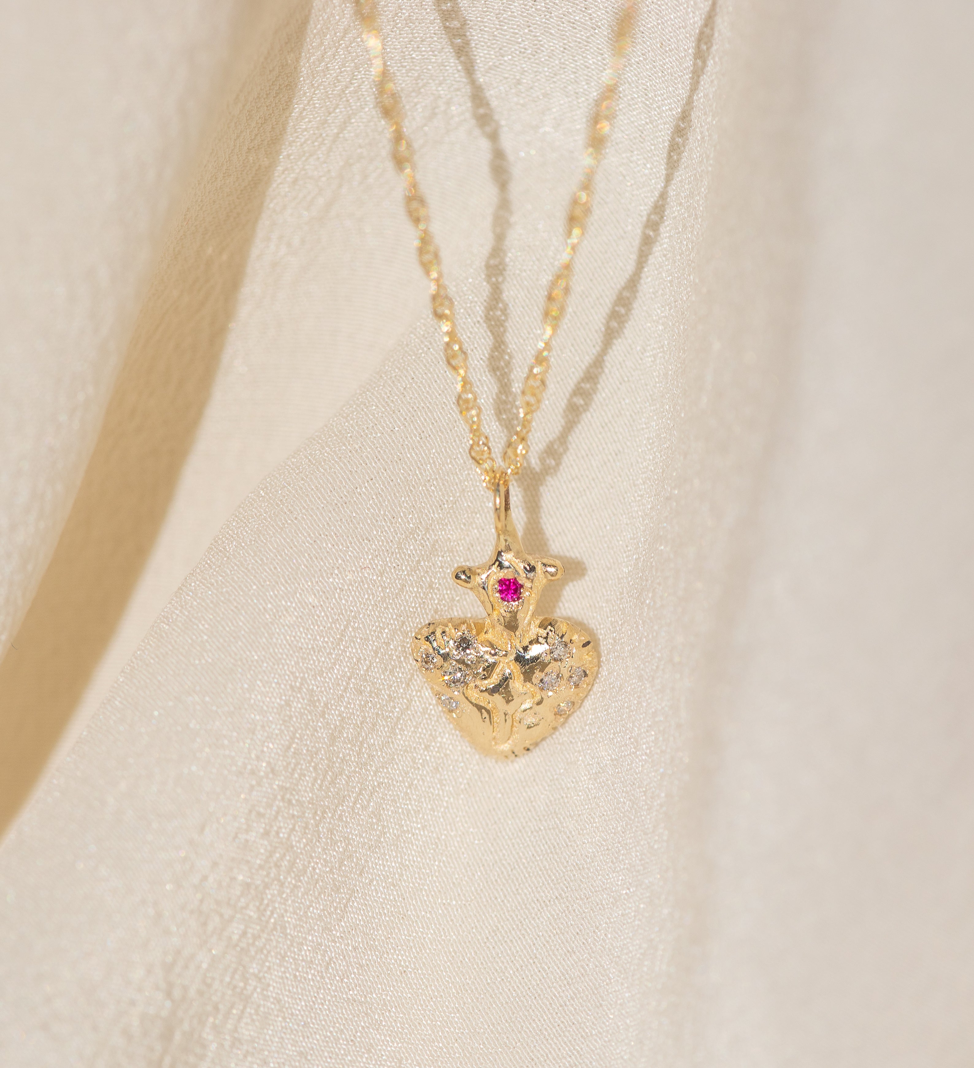 Gold heart-shaped necklace with a red gemstone on a beige background
