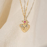 Gold necklace with a heart-shaped pendant featuring a red gemstone on a beige background