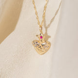 Gold heart-shaped pendant necklace with a red gemstone on a beige background