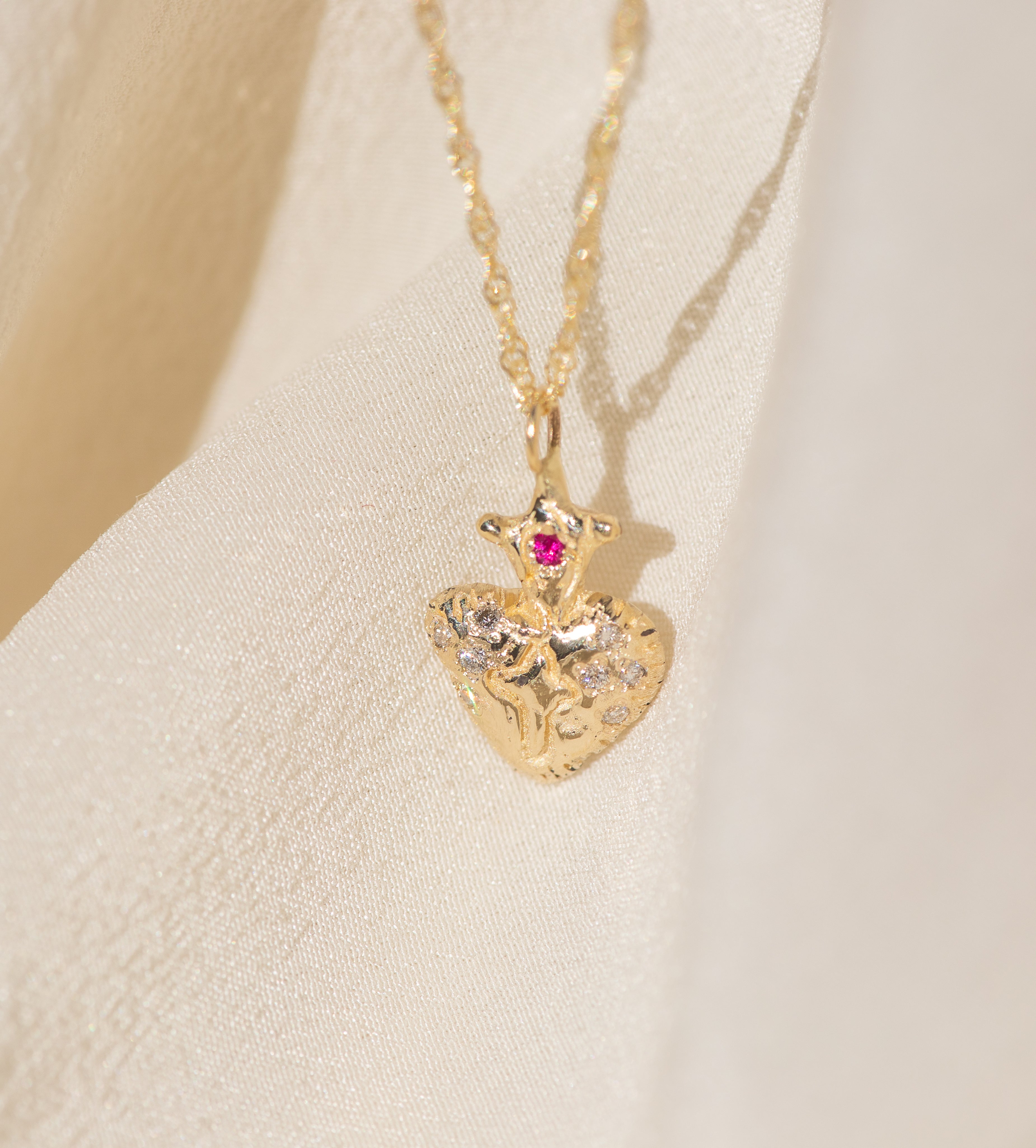 Gold heart-shaped pendant necklace with a red gemstone on a beige background