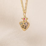 Gold heart-shaped pendant necklace with a red gemstone on a beige background