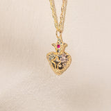 Gold heart-shaped pendant necklace with a red gemstone on a beige background