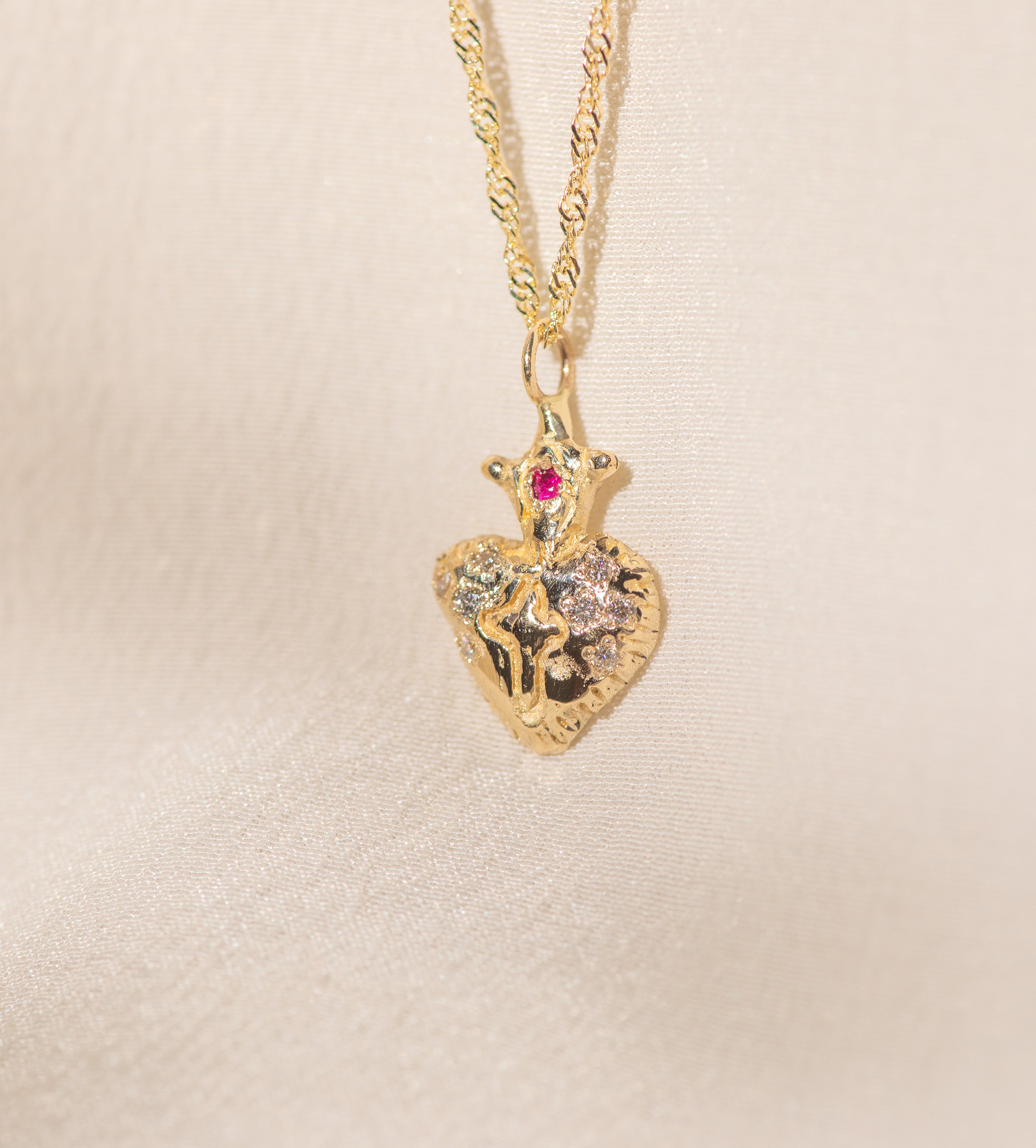 Gold heart-shaped pendant necklace with a red gemstone on a beige background