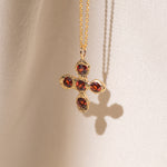 Gold necklace with a cross pendant featuring red garnet gemstones