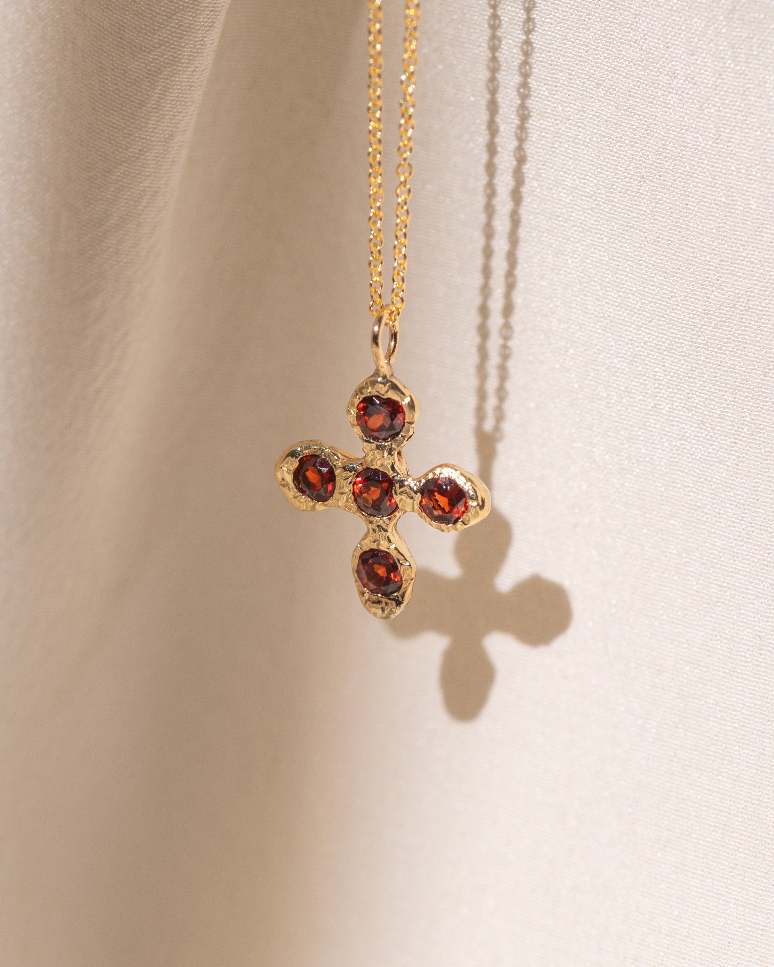 Gold necklace with a cross pendant featuring red garnet gemstones