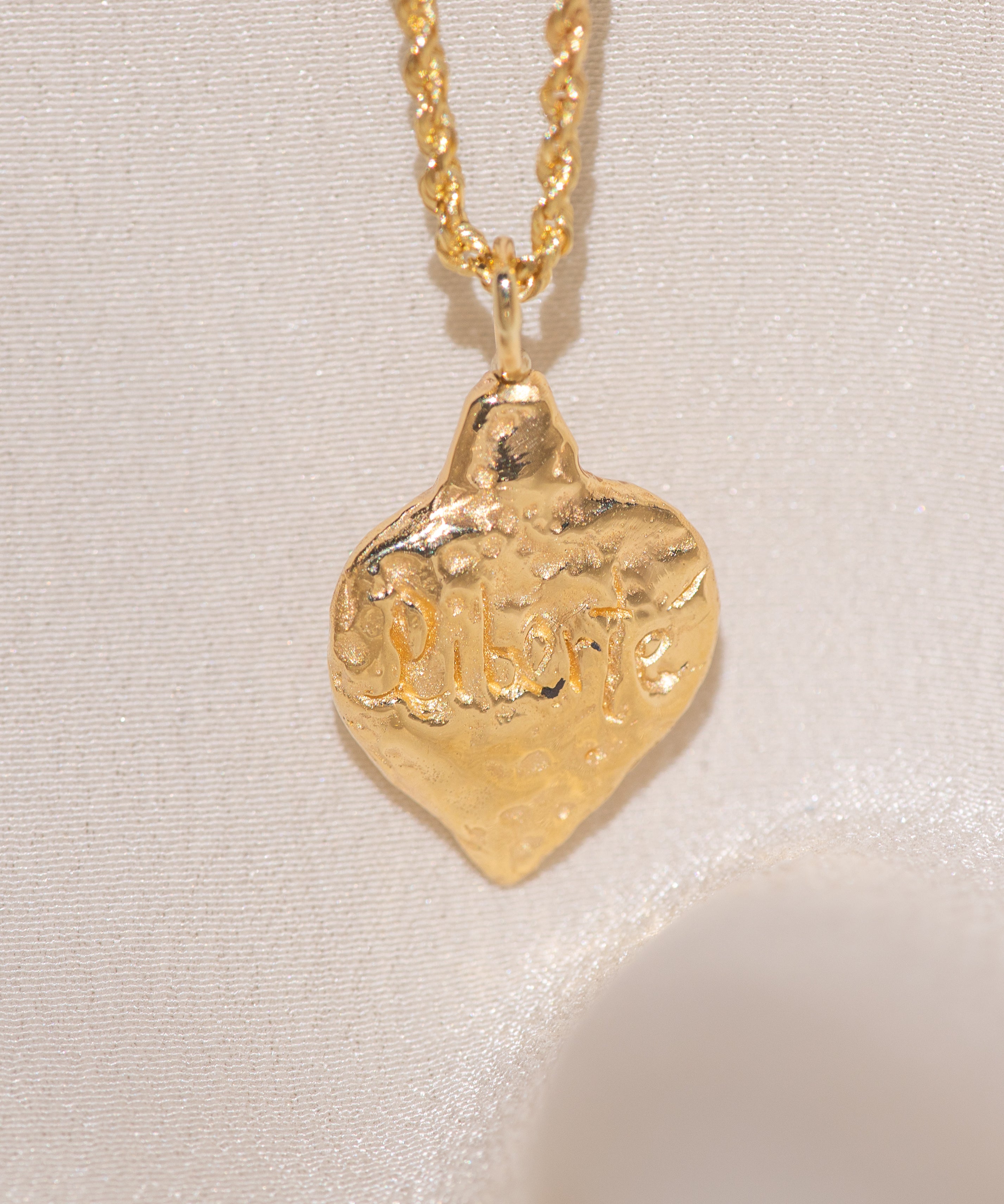 Gold heart-shaped medallion necklace featuring hand carved "liberty" in the back