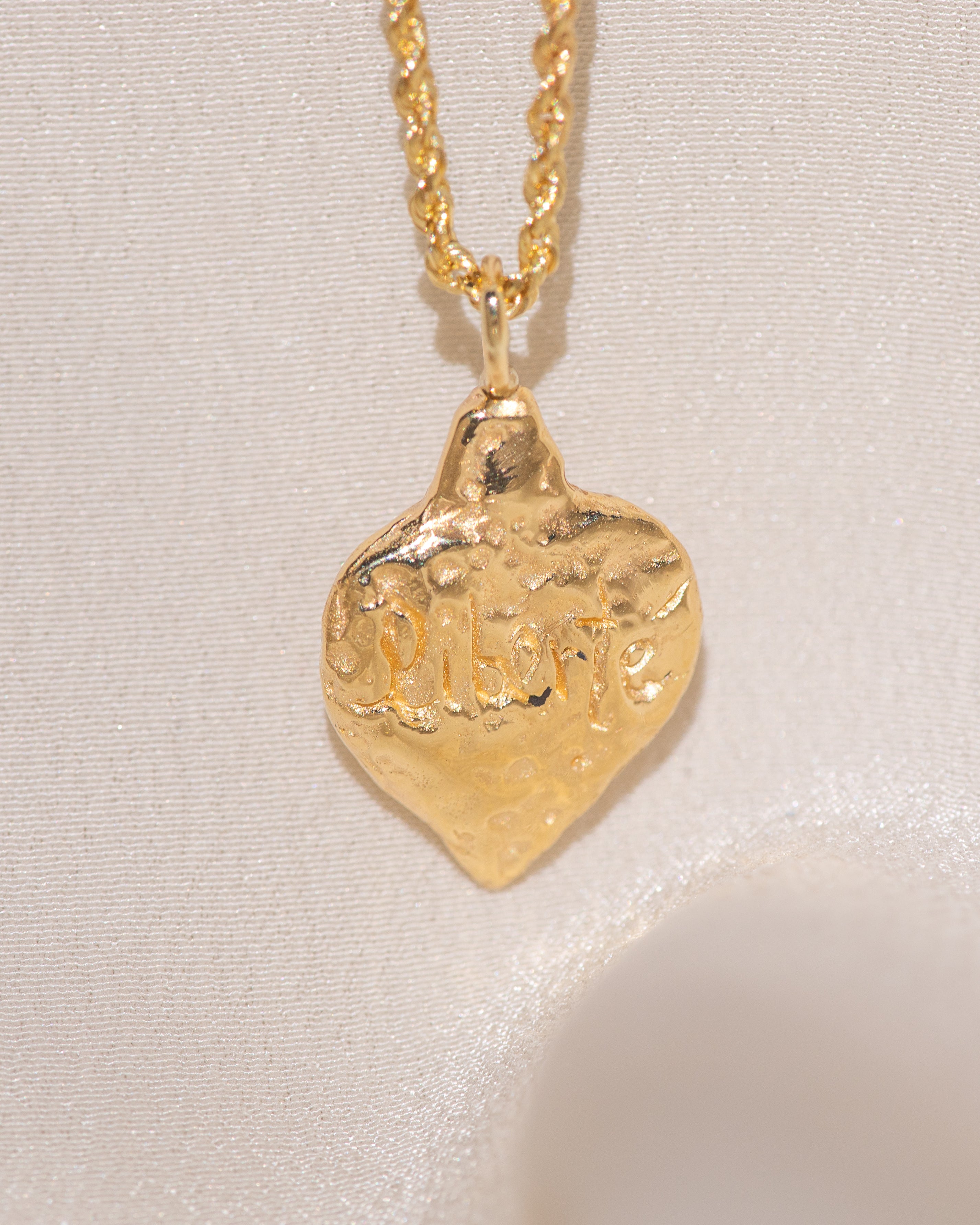 Gold heart-shaped medallion necklace featuring hand carved "liberty" in the back