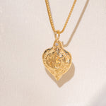 Gold heart-shaped medallion necklace featuring a white diamond and a dove